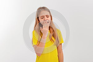 Tired teen girl closed eyes cover mouth with hand yawning feels weak bored, stands in casual yellow t shirt over white studio