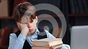 Tired teen schooler boy sleeping on desk laptop with stack of books learning homework at library