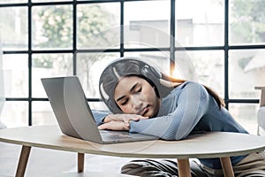 Tired teenage asian female student fell asleep at her desk, resting her head on her hand, during a lecture in home