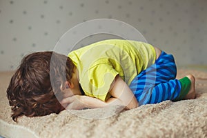 Tired toddler boy lying on the bed with his face down. Crying little kid