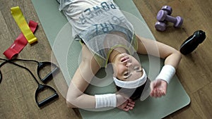 Tired of training in the fitness room, a young woman is resting lying on a karemat.