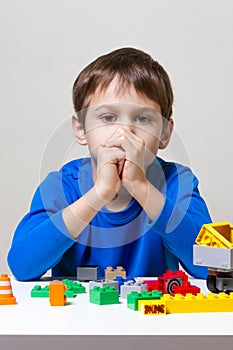 Tired unhappy child sitting and looking to colorful plastic construction toy blocks at the table