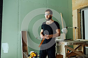 Tired unhappy man standing with corner ruler in rennovating apartment