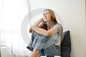 Tired and unhappy millennial Asian woman sitting in living room, feeling upset with herself