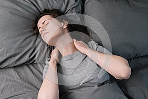 Tired unhappy young woman lying in bed in morning feels pain in neck after night sleep, massage tense neck muscles