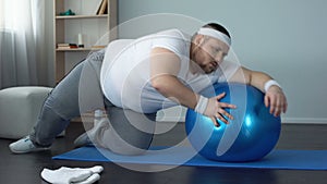 Tired unmotivated obese man lying on fitness ball, slimming fitness program