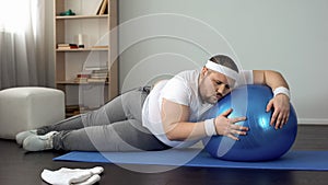 Tired unmotivated obese man lying on fitness ball, slimming fitness program