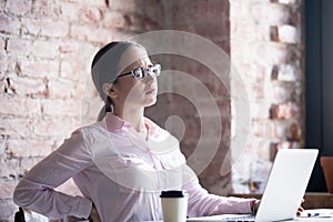 Tired upset woman suffering from backache at office desk