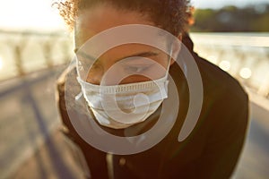 Tired woman. Close up photo of exhausted african female jogger in medical mask resting after run while standing on the
