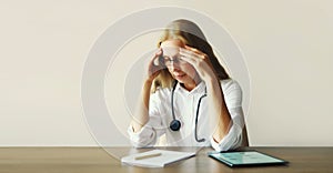 Tired woman doctor working with documents while sitting at desk in medical clinic office