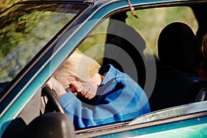 Tired woman driving a car. A middle-aged woman in her forties leaned over the steering wheel of a car. Fatigue, exhaustion, rest