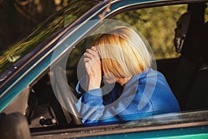 Tired woman driving a car. A middle-aged woman in her forties leaned over the steering wheel of a car. Fatigue, exhaustion, rest