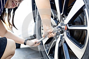 Tired woman with flat car tire,wrench in hands,trying to change wheel after a car breakdown,repairing with difficulty,accident
