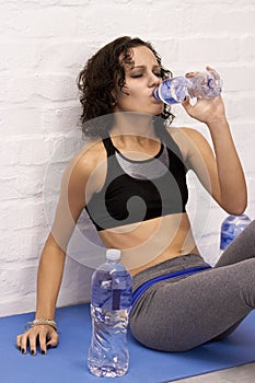 Tired woman, gym and drinking water on floor with eating disorder, anorexia or stress to lose weight. Girl, bottle and