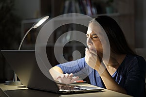 Tired woman with laptop yawning at night at home