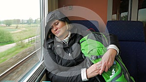 Tired woman rides on the train and sleeps against the window.