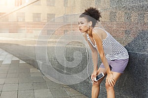 Tired woman runner is having break, standing near grey wall
