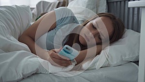 Tired woman with sad eyes using smartphone on bed at home