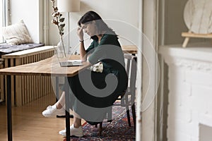 Tired woman sitting at table with laptop in home office