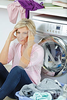 Tired woman sitting by washing machine