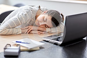 Tired woman sleeping on table with laptop at home