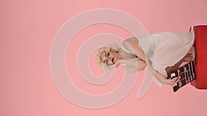 Tired woman squatting with clapper in hands. Woman looking like Marilyn Monroe squatting on red pedestal in studio on