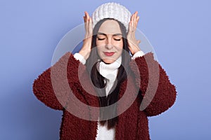 Tired woman touching her temples, girl with bright red lips feeling stress and terrible headache, female wearing coat and white