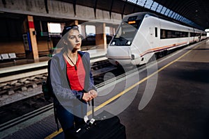 Tired woman traveler with bags and suitcase waiting on the peron of a train station.Traveling with train/metro.Last minute