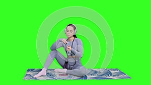 Tired woman after workout, drinking water, sitting on mat on the chroma key