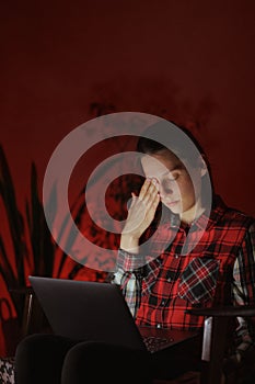 tired woman works on laptop in home office in the evening