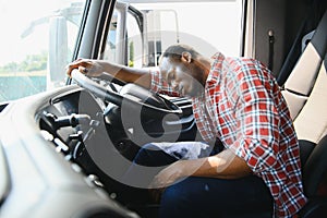 Tired of work. Sitting in the cabin. Young african american truck driver is with his vehicle at daytime.