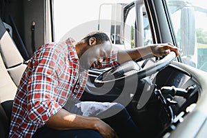Tired of work. Sitting in the cabin. Young african american truck driver is with his vehicle at daytime.