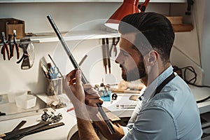 Tired from working so late. Side view of bearded male jeweler working with a new ring with jeweler`s tool