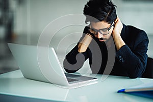 Tired and worried indian business man at workplace in office holding his head on hands