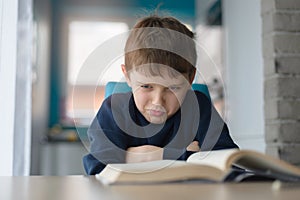 Tired 8 years old boy doing his homework at the table