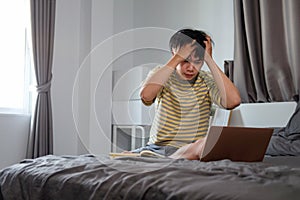 Tired young asian man working with computer laptop on his bed