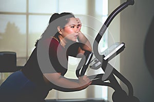 Tired young Asian overweight women exercising on elliptical trainer in the gym. Weight loss workout, healthy lifestyle concept