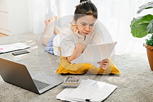 Tired young Asian woman working for laptop with graph documents from home on the carpet.