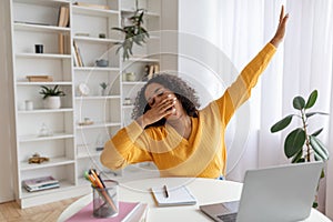 Tired young black female student yawning in front of laptop during online lesson at home