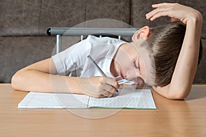 Tired young boy lay down on a desk writing down homework or preparing for an exam, front view