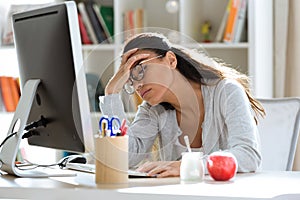 Tired young business woman having headache while working with computer in the office