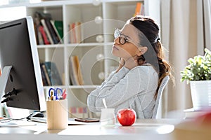 Tired young business woman having neck and back pain while working with computer in the office