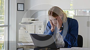 Tired young businessman feeling stressed and overwhelmed sitting in modern office with laptop