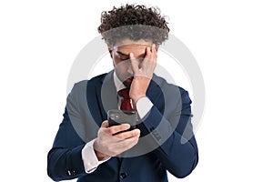 Tired young businessman in suit reading emails and face palming