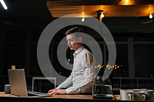 Tired young businessman working laptop in evening office. Focused business man reading computer standing by desk