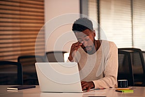 Tired Young Businessman Working Late Sitting At Desk With Laptop In Modern Open Plan Office