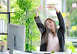 Tired young businesswoman sitting in the office stretching her arms above her head for relaxation after long hours of working on a