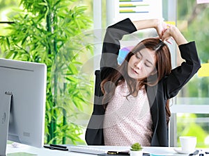 Tired young businesswoman sitting in the office stretching her arms above her head for relaxation after long hours of working on a