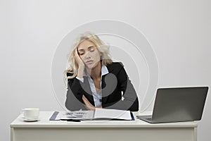 Tired young businesswoman sleeping on her desk in front of laptop, overworking, feeling exhausted at office