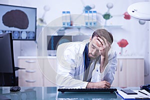 Tired young doctor trying to focus holding his head sitting down in the office